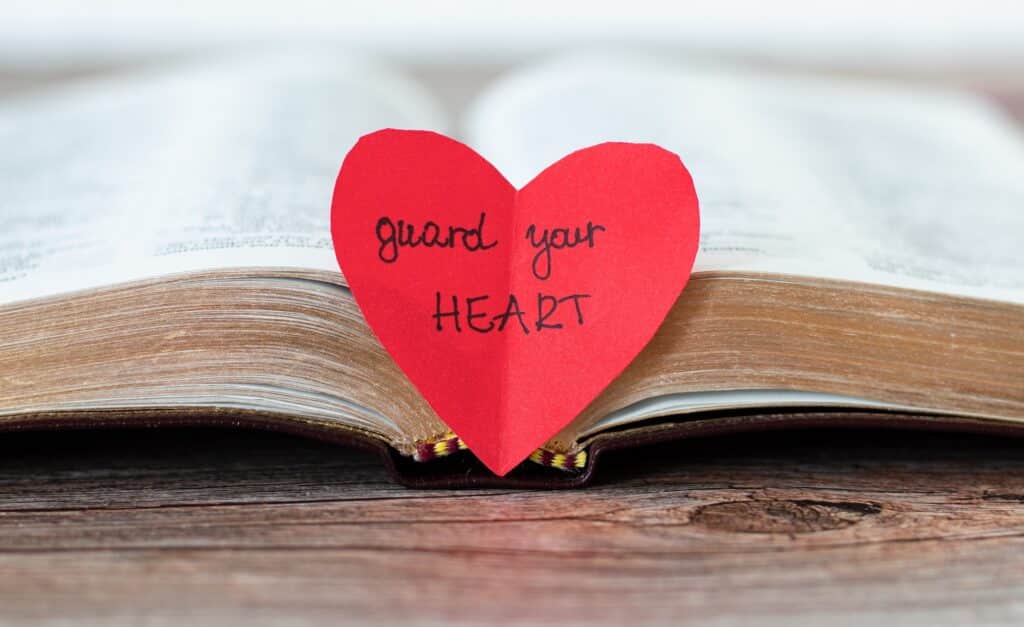 Photo of a Bible and a cut-out paper heart that quotes Proverbs 4:23